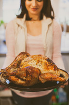 a woman holding a roasted turkey 