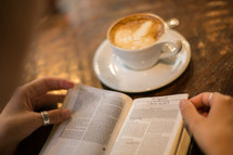 a woman reading a Bible sitting at a table in a coffee shop 