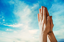 Hands praying with sky in the background