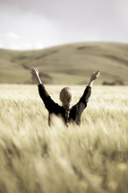 a woman with raised hands standing in a field of wheat 