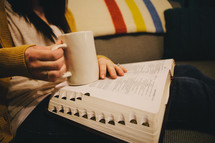 A woman holding a coffee mug and reading a Bible. 