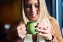 a woman in a sweater and scarf drinking coffee