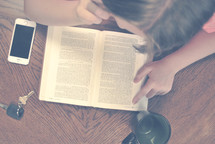 woman reading a Bible with a coffee mug, car keys, and cellphone on the table 