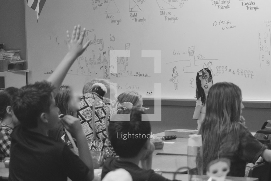 kids in a classroom with hands raised answering questions 