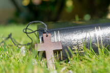 wooden cross necklace and Bible in the grass