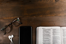 reading glasses, iPhone with earbuds, and open Bible 