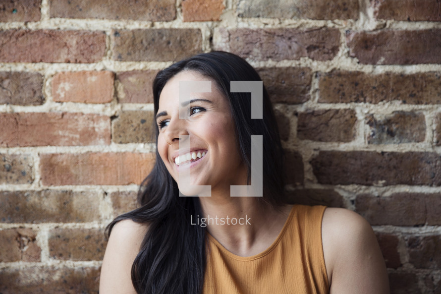 A smiling young woman sitting against a brick wall.