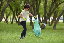 a boy picking up trash in a park 