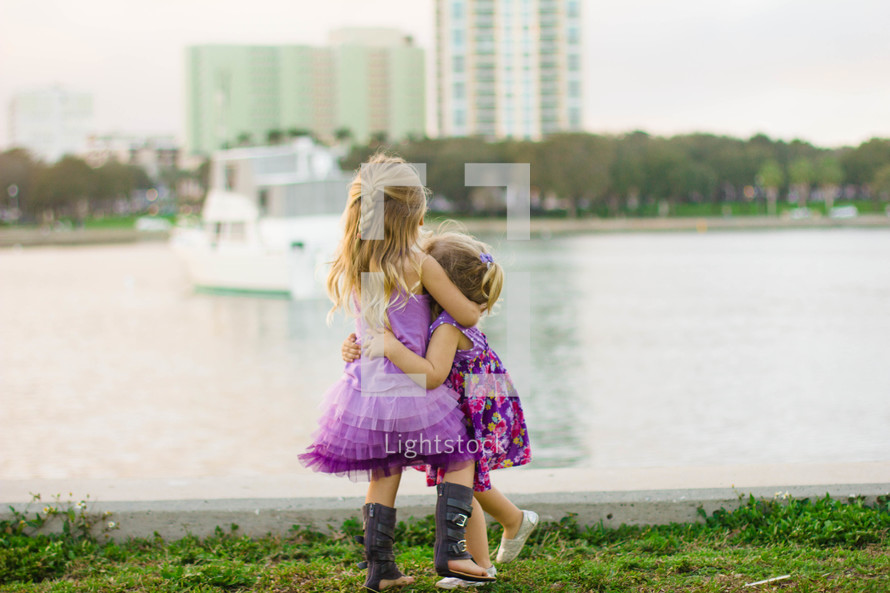 Two little girls embracing by a lake.