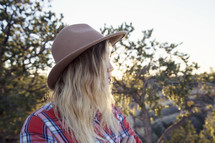 blonde woman in a plaid shirt and hat standing outdoors 
