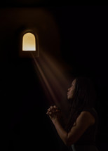 sunlight through a small window shining on a woman's face as she prays
