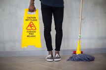 woman holding a mop and wet floor sign 