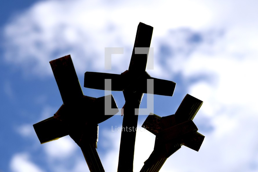 silhouettes of three palm crosses against a blue sky 