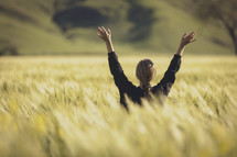 a woman standing in a field of wheat with raised hands 