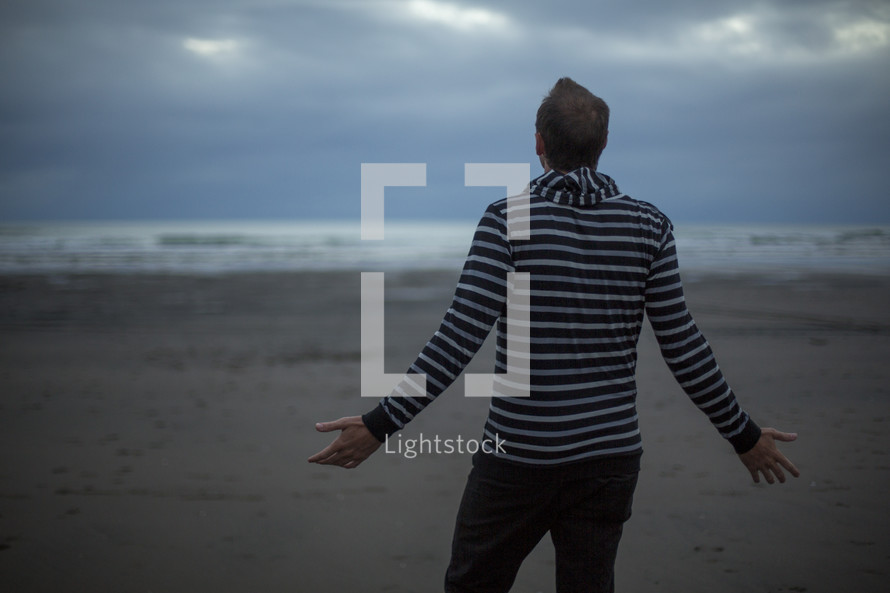 man standing on a beach with outstretched arms 