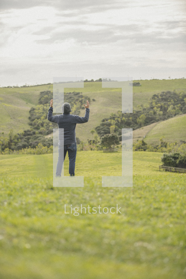 man standing in a field with raised arms 