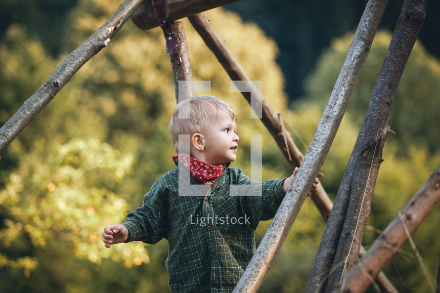 Adorable Cute Blond Boy in Nature between Wooden Logs
