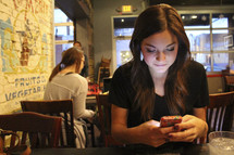  a young woman sitting at a diner table texting 