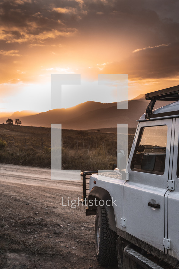 Jeep on a dirt road and mountains at sunset 