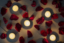 Burning candles among red rose petals.