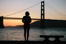 Silhouette of a woman looking at a suspension bridge.