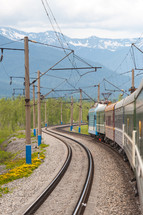 Power lines near a train on railroad tracks near a mountain range.