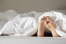 Child's feet sticking out from the blanket at the end of the bed.
