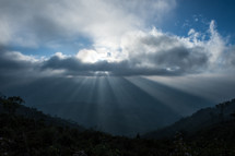 Rays of sunlight on a valley, through the clouds.