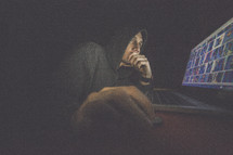 A man in a hooded sweatshirt intently studies a computer screen.