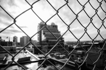 city buildings through a chain linked fence 