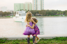 Two little girls embracing by a lake.