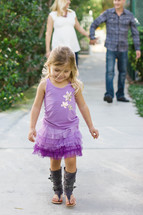 A little girl walking along the sidewalk in front of her parents.