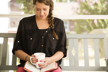 woman praying sitting on a porch swing with a Bible and coffee mug