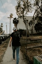 teen boy with a book bag walking down a sidewalk 
