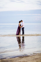 A man and woman holding hands on a sand bar surrounded by water.