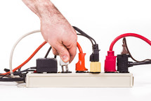 A hand plugging in plugs into a power strip 