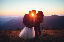 a bride and groom on a mountaintop at sunset 