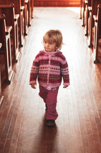 a toddler walking in the aisle of an empty church 