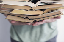 man holding open books stacked in a pile.