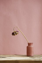 a wilted flower in a vase on a wood table.