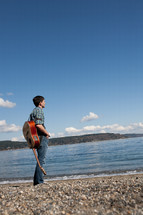 man with a guitar on his back standing in front of a lake