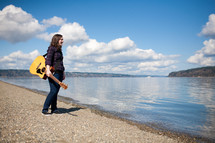 woman holding a guitar standing by a lake 