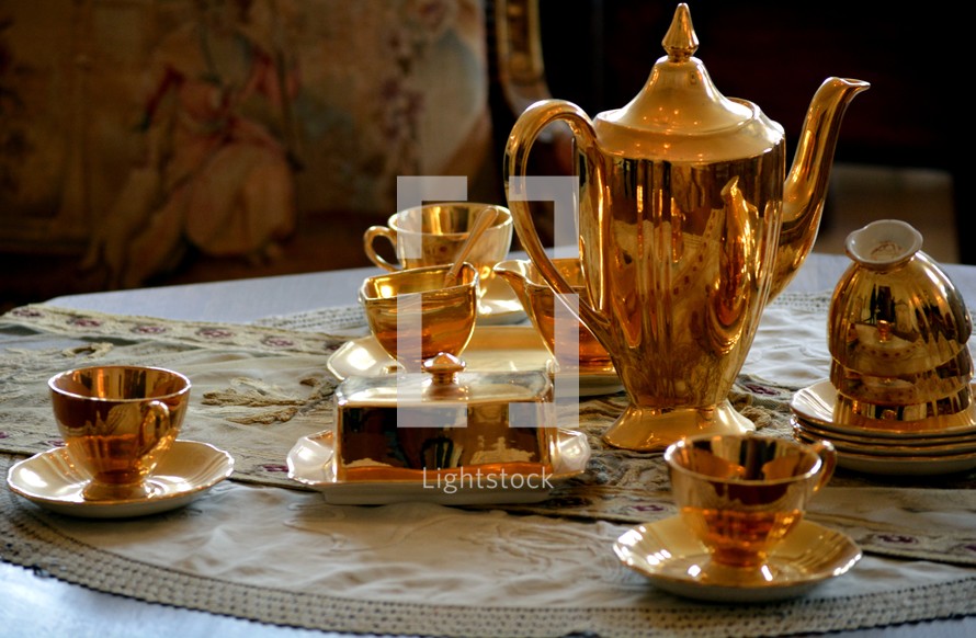 gold tea pot and cups on a table at a tea party 