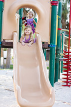 Two little girls on a park slide.