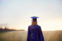 female graduate walking through a field 