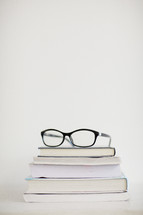 A pair of eyeglasses on top of a stack of books.