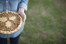 A woman stands holding a freshly baked pie.