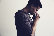 man standing in prayer with head bowed and praying hands 