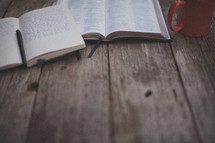An open Bible and notebook next to an orange coffee mug