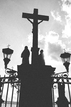 Silhouette of Jesus om the cross with statues in a courtyard.